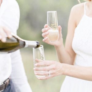 A woman holds out two customized champagne glasses and a man fills them up.
