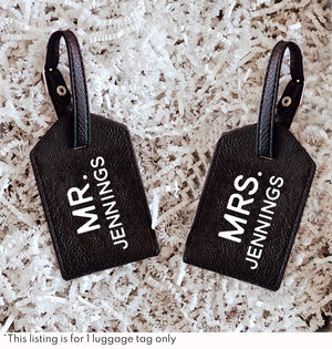 Two black luggage tags with white lettering customized for a Mr. & Mrs.