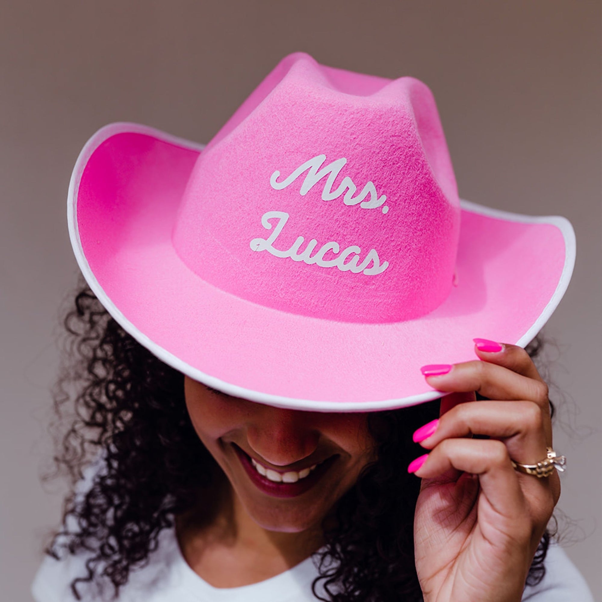 A pink cowboy hat is customized with white font which reads "Mrs. Johnson".