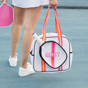 A woman holds a pink and orange pickleball bag with a name embroidered on it