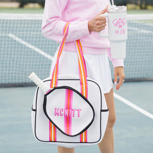 A woman holds a pink and orange striped pickleball bag and a white 40 oz with a pink pickleball design