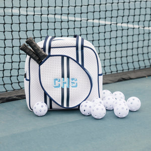 A navy pickleball bag is embroidered with a blue monogram and placed on a court.