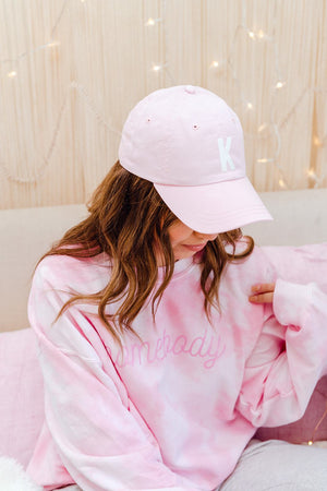 A pink hat is monogrammed with white text