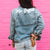 A woman stands in front of a pink wall wearing a customized jean jacket.
