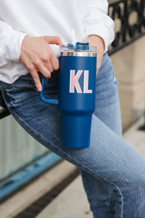 A woman wearing jeans holds a navy blue tumbler with a monogram