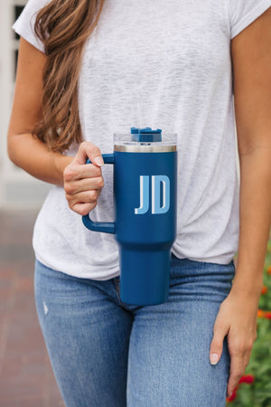 A woman wearing jeans holds a navy blue tumbler that reads "JD"