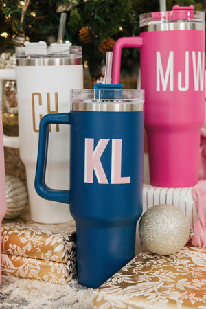 Three tumblers in white, hot pink, and navy sit under a Christmas tree