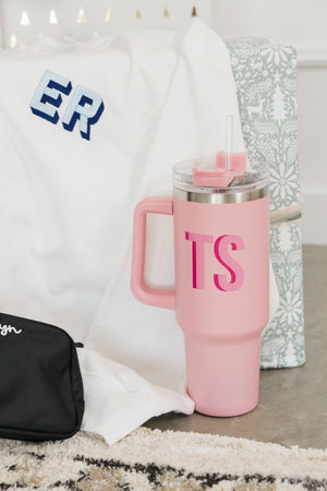 A pink, monogrammed tumbler sits next to other monogrammed items