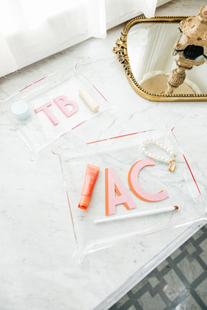 A set of acrylic trays are monogrammed and placed on a bathroom counter.
