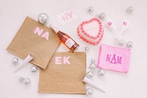 An assortment of pink monogrammed products are laid out with a pink heart cake, rose, and disco balls.