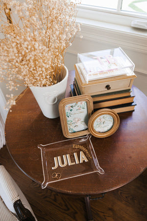An acrylic tray with a beige and white name decorates a wooden table 