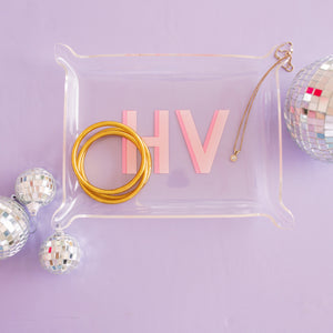 An acrylic tray with a pink monogram is placed on a purple background with disco balls.
