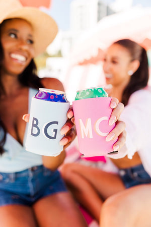 Two women hold out can coolers with monograms on them