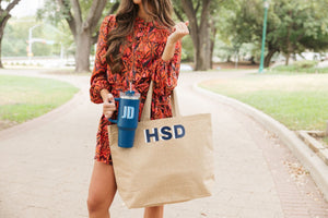A woman in a red dress holds a customized tumbler and monogrammed jute tote