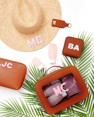 An array of tan leather products are customized with matching pink monograms.