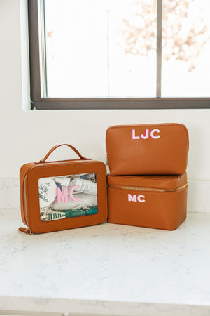 A group of tan leather products with pink monograms are paired together in a bathroom.