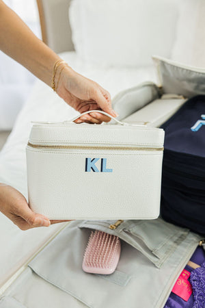 A person holds up a white train case with a light blue and navy monogram.