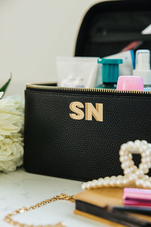 A black train case is personalized with a neutral colored monogram on the front.