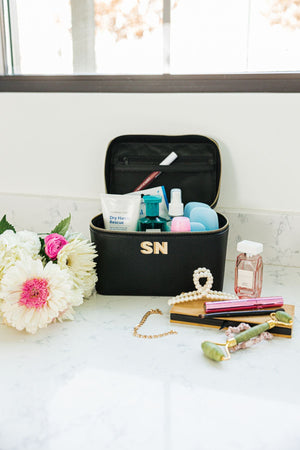 A personalized black leather train case is propped open by toiletries.