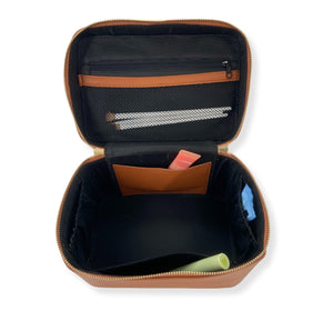 A tan train case is opened to show off the interior pockets on each  side and a zipper pouch attached to the lid.