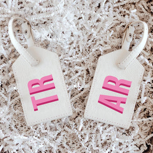A white luggage tag is customized with a pink monogram