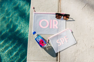 2 pink pool bags with pink monograms lay by the edge of the pool with a pair of sunglasses and a water bottle.