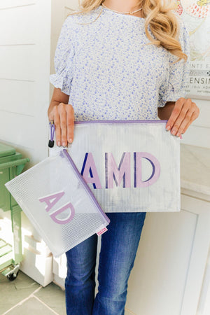 A woman holds up two purple zipper pool bags with purple monograms on them.