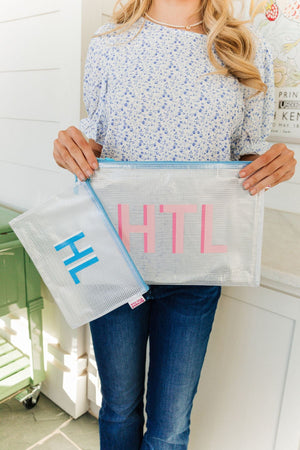 A woman holds up two blue zipper pool bags with pink and blue monograms on them.