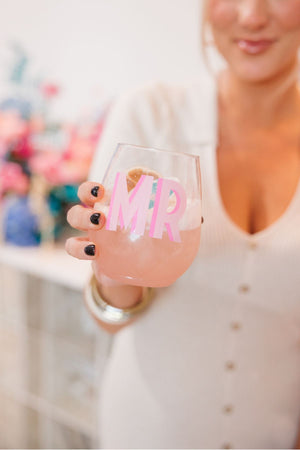 A person holding a stemless wine glass with pink shadowed initials on it