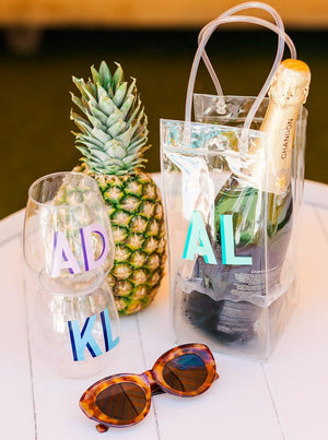 Two monogrammed wine glasses sit next to a bottle of wine in a custom wine tote