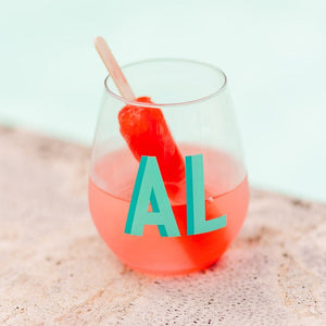 A red popsicle melts in a cocktail contained in a monogrammed wine glass