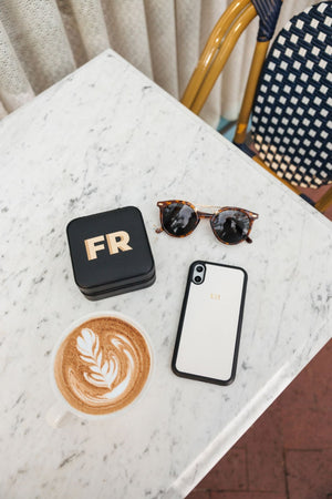 A monogrammed phone case and travel jewelry case sit next to a latte
