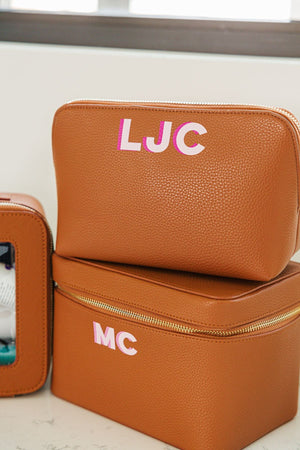 A tan leather pouch and train case are monogrammed with pink initials.