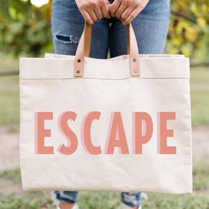 A woman holds a weekender bag that reads "Escape"