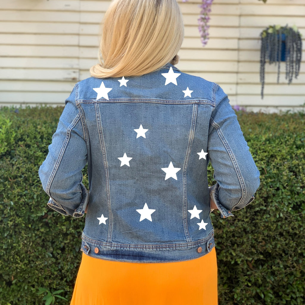 A woman in a jean jacket with white stars stands outside.
