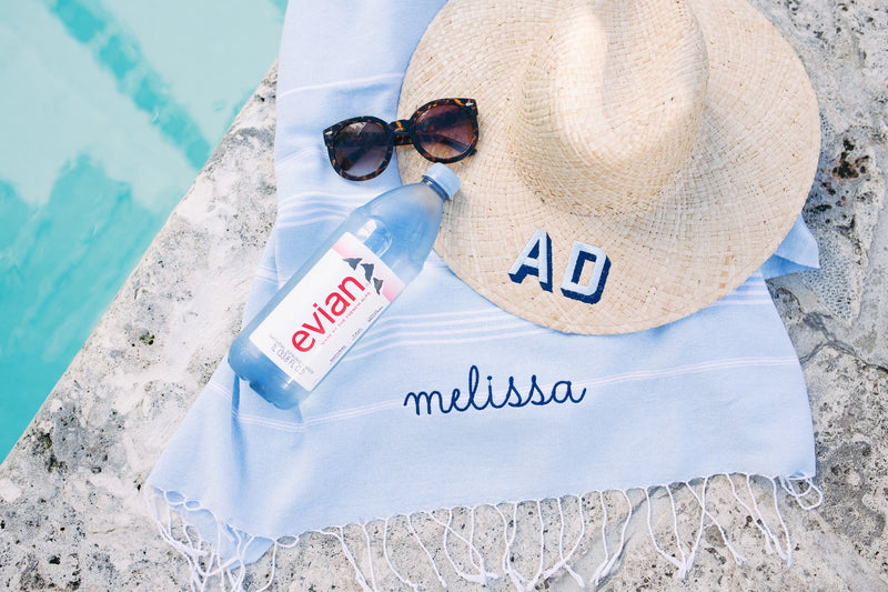 An embroidered beach hat and towel lay in the sand