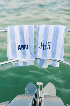 Two blue cabana towels are placed hanging over a boat railing and are customized with navy monograms.
