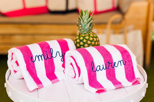 Two pink cabana towels are embroidered with custom names in a script font.
