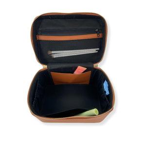 A tan train case is opened to show off the interior pockets on each side and a zipper pouch attached to the lid.