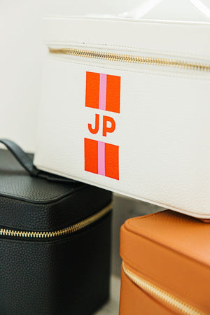 A white train case is customized with a pink and orange stripe and monogram.