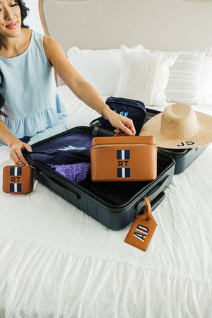 A person packs a suitcase with personalized products like a leather train case and jewelry case with navy stripe monograms.