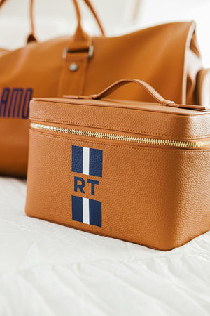 A tan leather train case is customized with a navy stripe monogram.