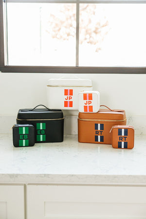 A group of matching train cases and jewelry cases are set on a bathroom counter.