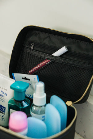 A black train case is opened and filled with products, Inside there is a pocket on the lid with a zipper.