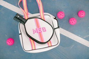 A pink and white pickleball bag is laid on a court and customized with a pink monogram.