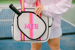 A woman unzips a pink and white pickleball bag which is customized with a pink monogram on the front.