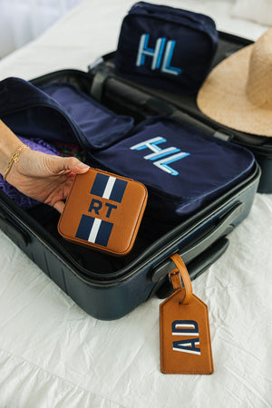 A tan jewelry case is personalized with a white and navy monogram and packed into a suitcase