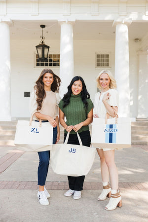 Three women hold different monogrammed totes including a weekender
