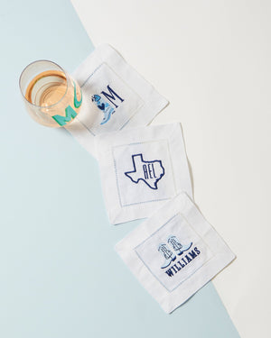 Three customized napkins are paired together with blue embroidered designs.