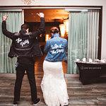 A husband wears a black jean jacket that says "The Party" and his wife wears a blue jean jacket that says "Wife of the Party". 